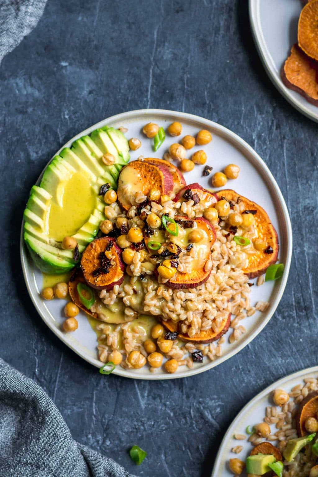 Roasted sweet potato and farro salad with garlicky chickpeas with sun dried tomatoes, avocado, and a lemon vinaigrette. Garnished with sliced scallion greens.