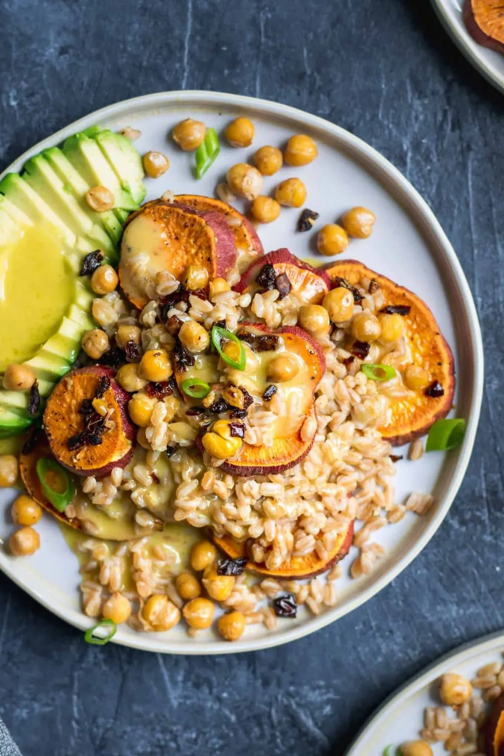 Roasted sweet potato and farro salad with garlicky chickpeas with sun dried tomatoes, avocado, and a lemon vinaigrette. Garnished with sliced scallion greens.