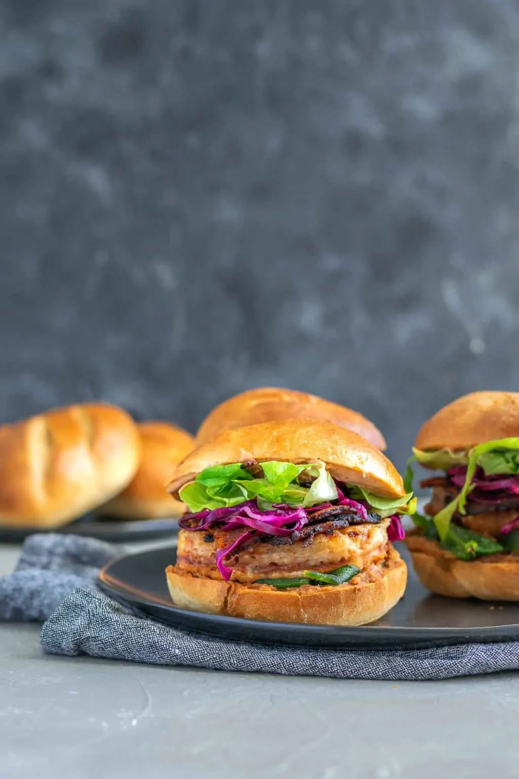 Vegan battered tofu Mexican tortas, 3 on a plate with a plate of rolls in the background