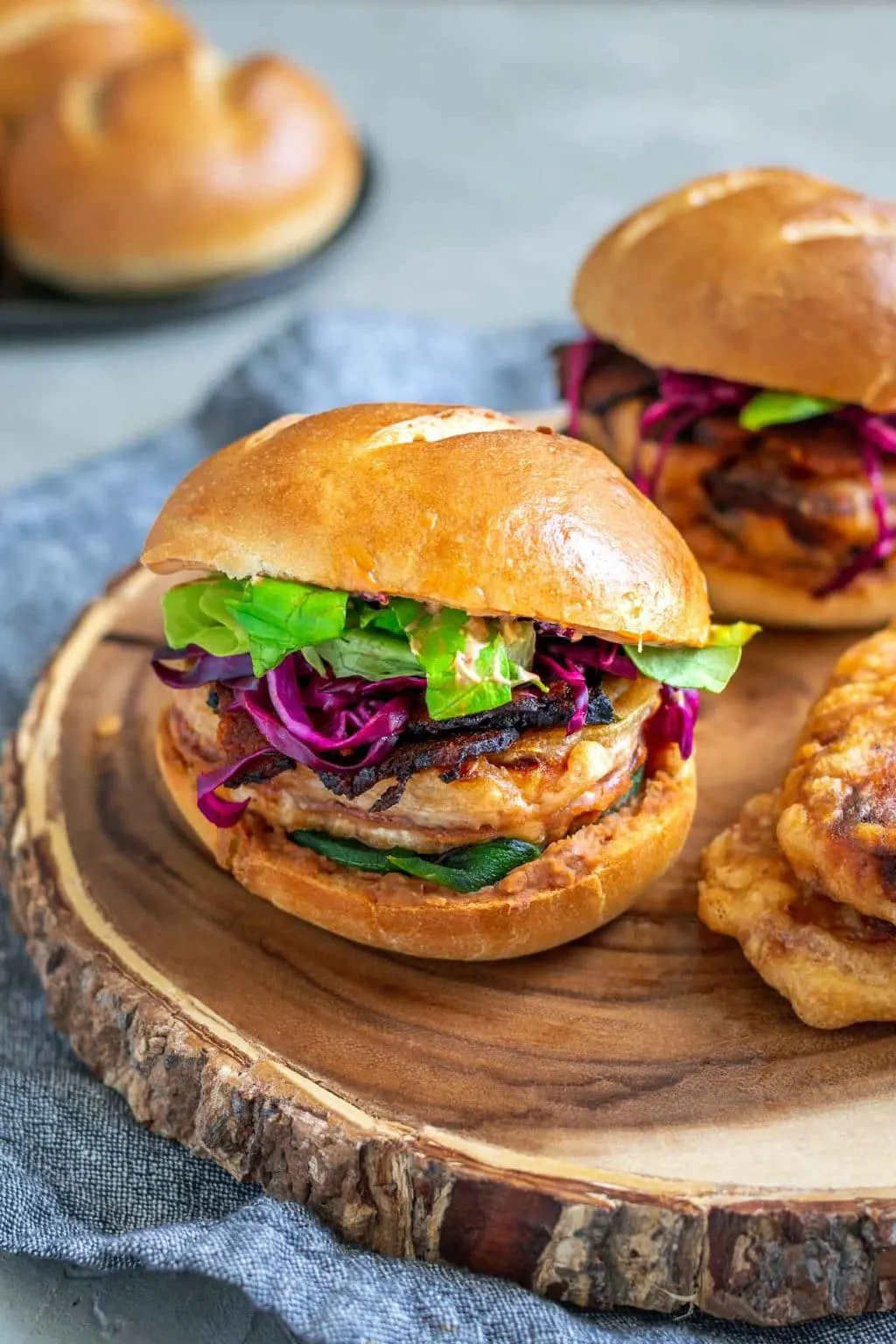 Vegan battered tofu Mexican tortas, close up of the filling from a slight angle with two tofu steaks stacked next to the sandwiches and extra rolls in the background