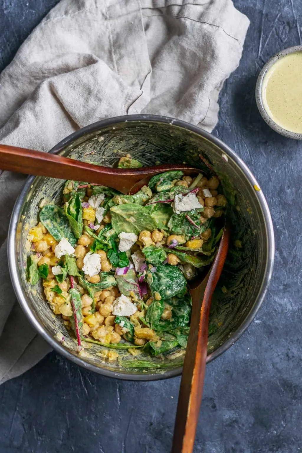 Curried chickpea and mango salad with vegan queso fresco being tossed in a mixing bowl with wooden spoons.