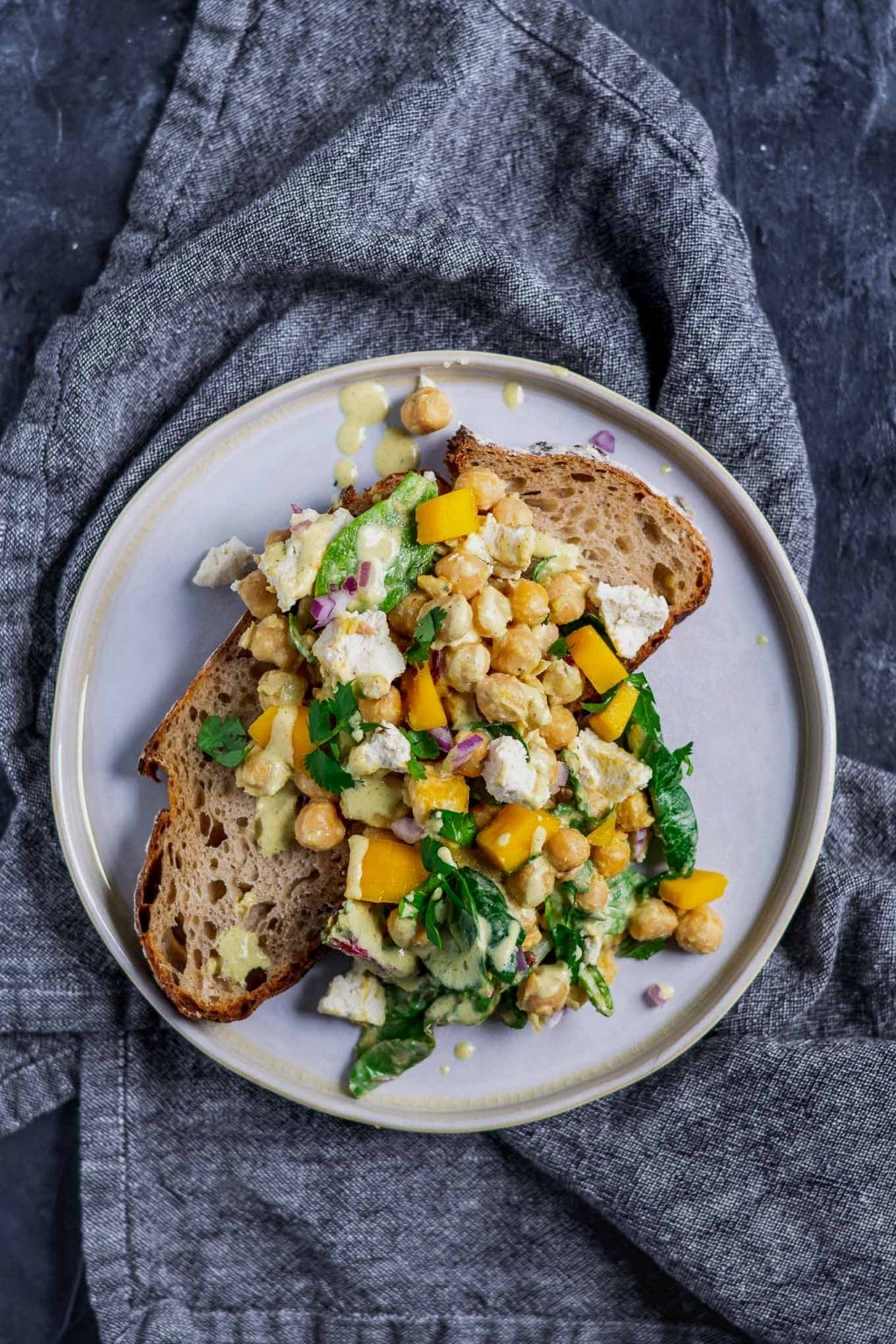 Curried chickpea and mango salad with vegan queso fresco served over a slice of toast with extra dressing drizzled on top