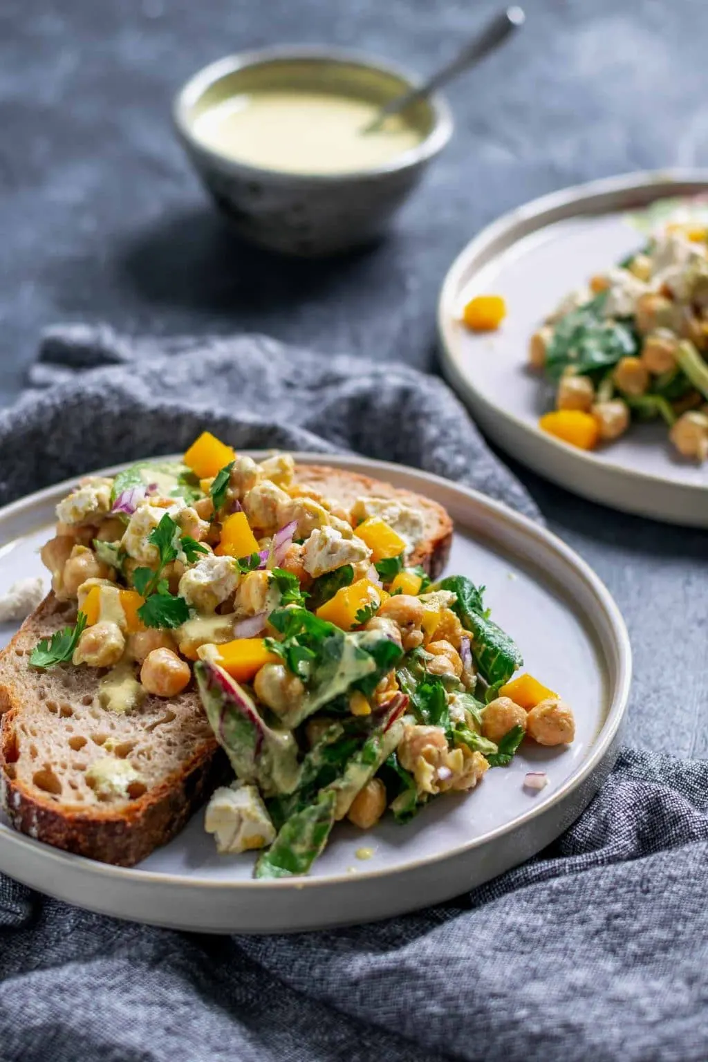 Side view of curried chickpea and mango salad with vegan queso fresco served over a slice of toast.