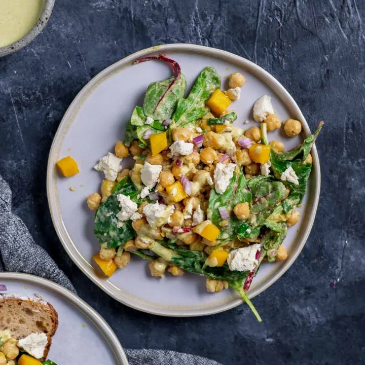 Curried chickpea and mango salad with vegan queso fresco. Extra dressing in a bowl in top corner and a second plate of the salad with a slice of toast