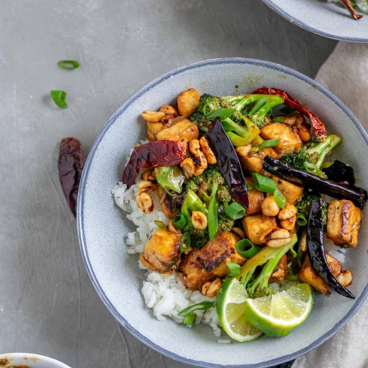 vegan kung pao tofu with broccoli and jasmine rice. Garnished with lime wedges and scallion greens