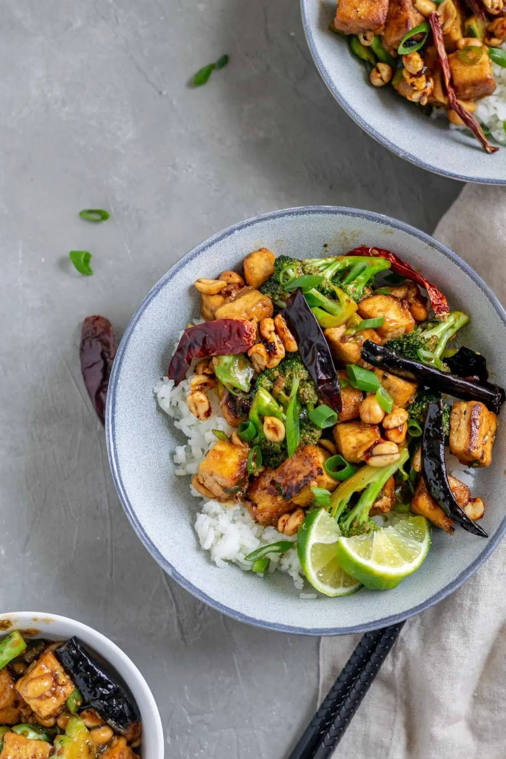 vegan kung pao tofu with broccoli and jasmine rice. Garnished with lime wedges and scallion greens