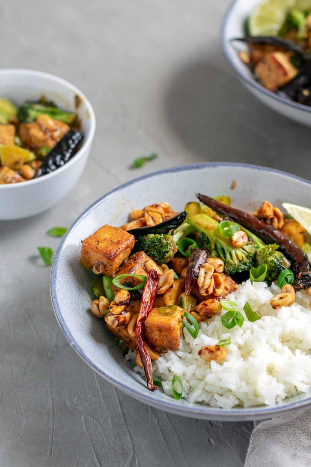 vegan kung pao tofu with broccoli and jasmine rice. Garnished with lime wedges and scallion greens. Angled view.