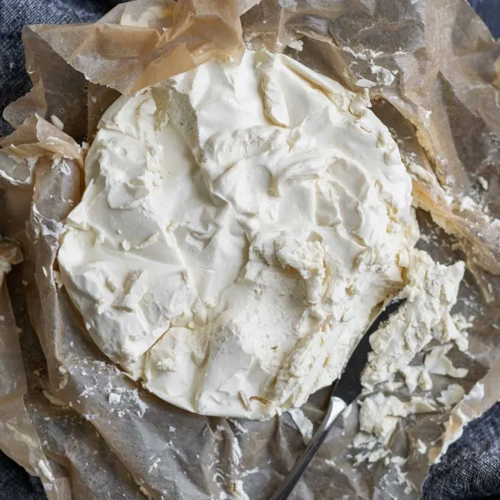 Easy homemade vegan queso fresco on crumpled parchment paper. Overhead view with a knife crumbling off some of the cheese.