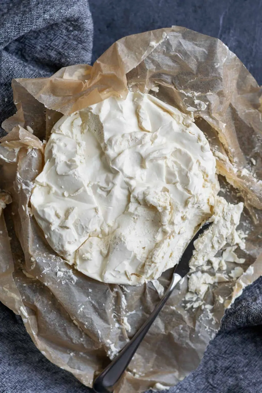 Easy homemade vegan queso fresco on crumpled parchment paper. Overhead view with a knife crumbling off some of the cheese.