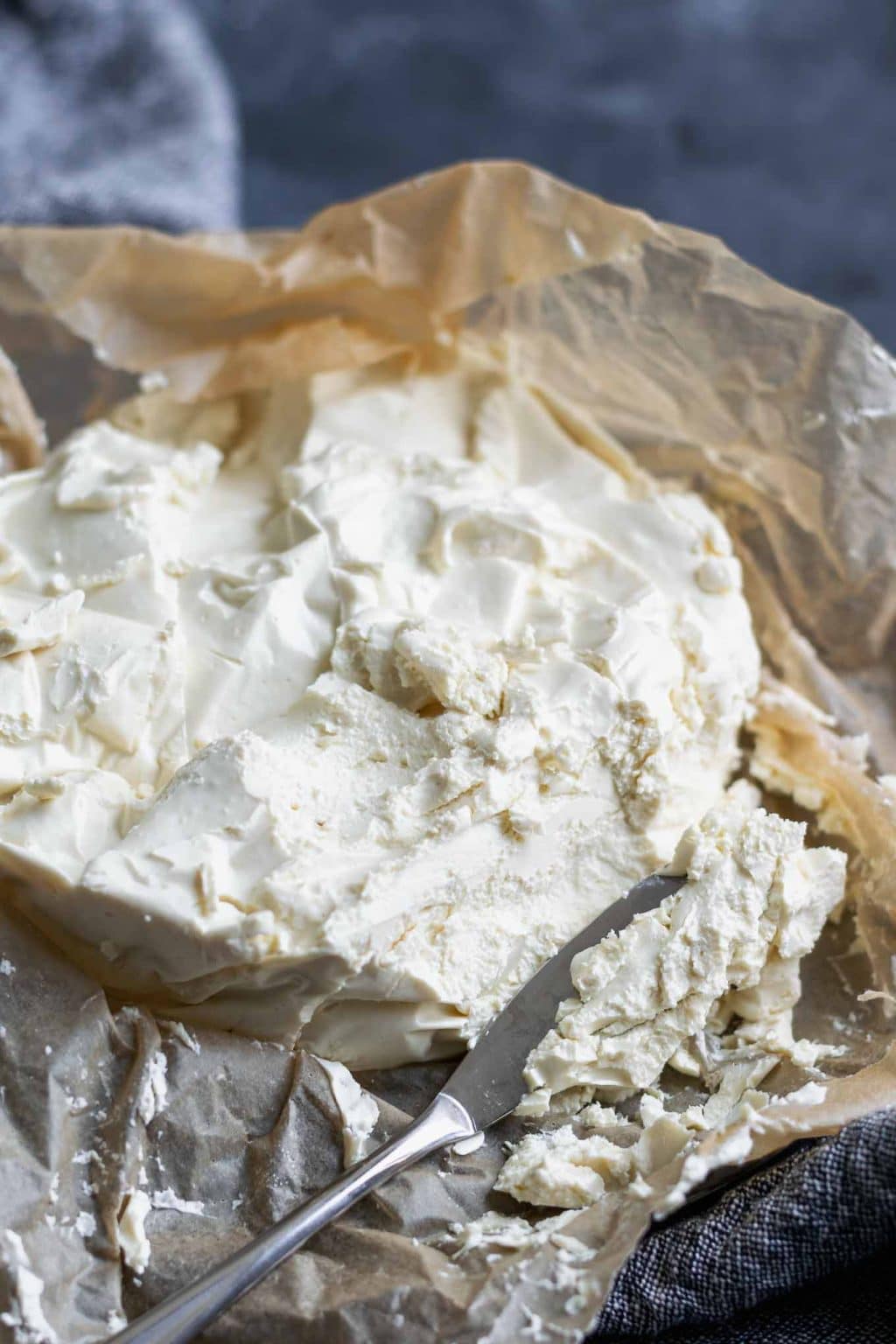 Easy homemade vegan queso fresco on crumpled parchment paper. Angled view with a knife crumbling off some of the cheese.