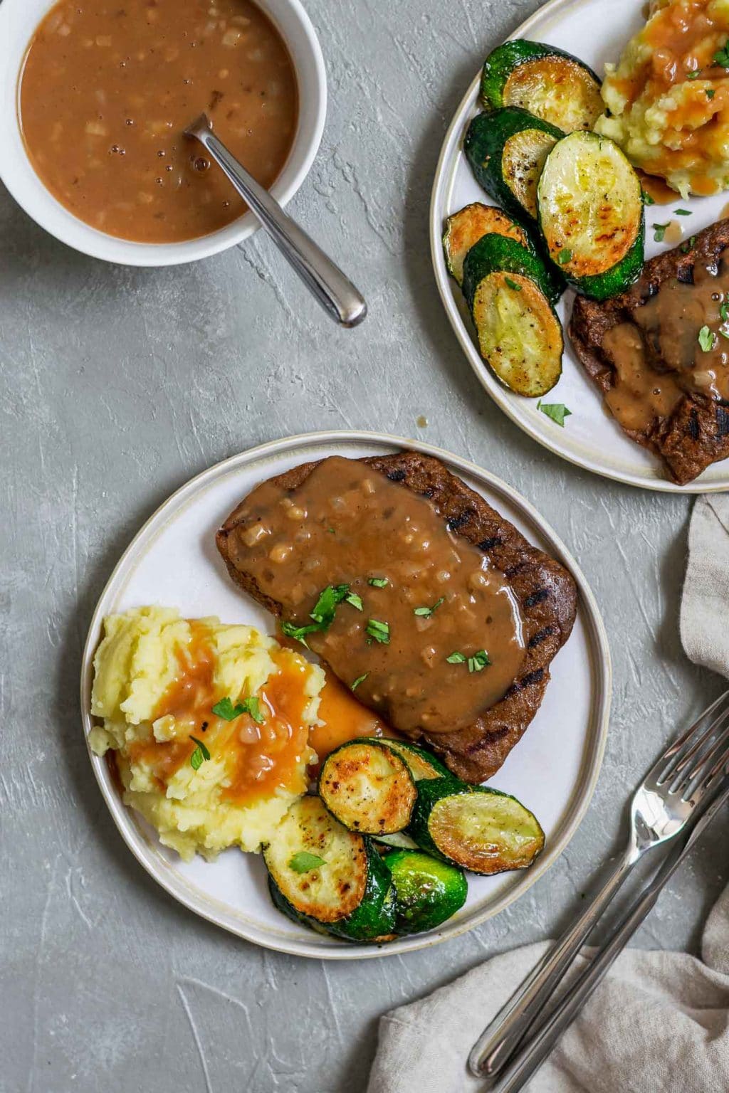 Steaks de seitan maison grillés avec purée de pommes de terre et sauce aux échalotes avec courgettes sautées, garnis de persil, et sauce supplémentaire sur le côté