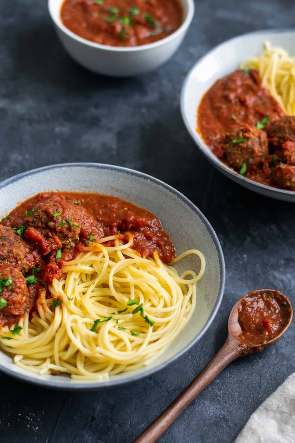 Spaghetti with roasted eggplant marinara and vegan lentil meatballs garnished with minced parsley. Angled shot.