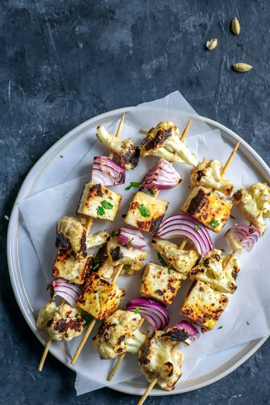 Afghan cauliflower and tofu tikka kebab skewers served on a plate with cardamom pods in one corner