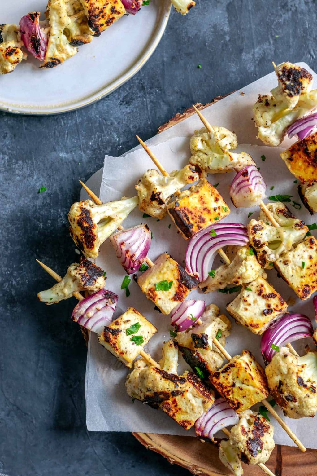 Afghan cauliflower and tofu tikka kebab skewers on a wooden platter with one served on a plate