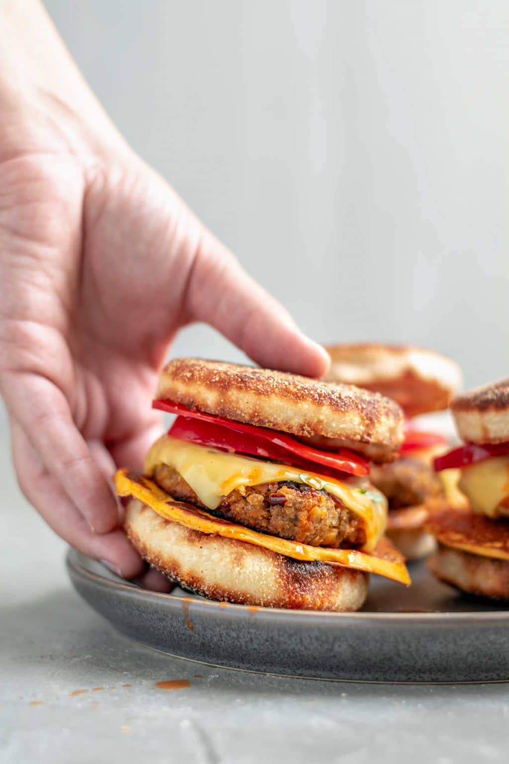 vegan breakfast egg and sausage muffins, picking one sandwich off a plate