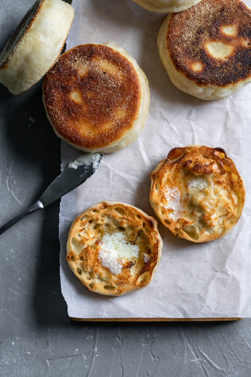 Homemade english muffins with a dab of vegan butter melting on top of one that has been cut open