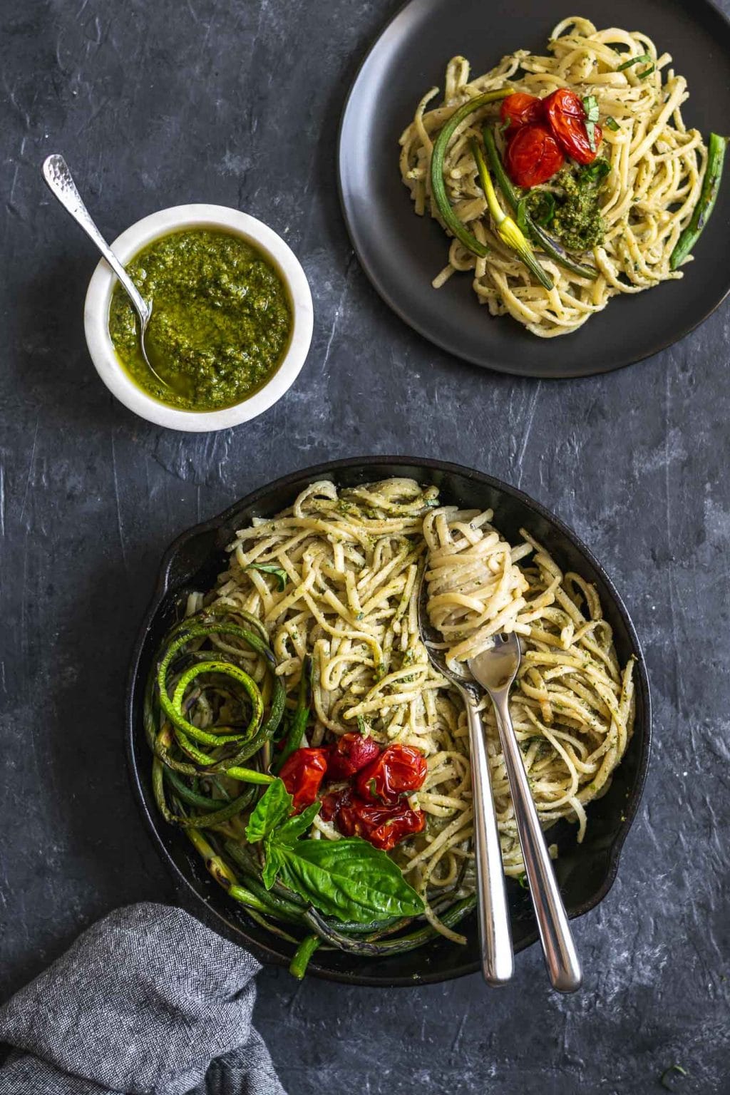 vegan garlic pesto alfredo pasta with grilled garlic scapes and roasted cherry tomatoes in a skillet with one plate served