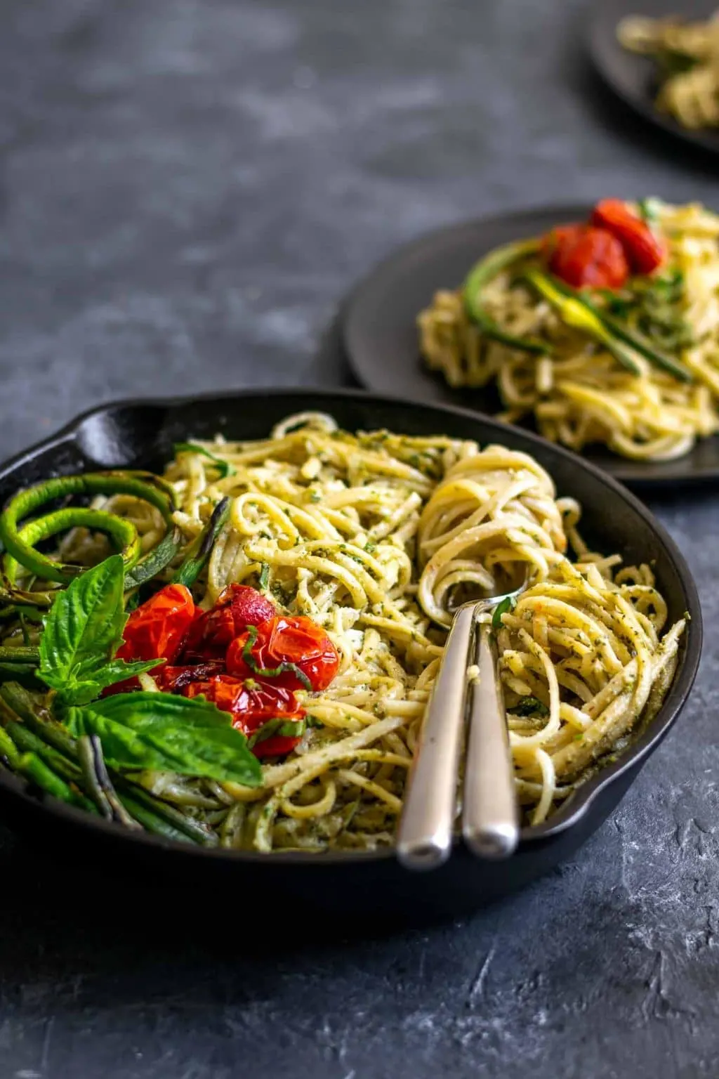 vegan garlic pesto alfredo pasta with grilled garlic scapes and roasted cherry tomatoes in a skillet with a couple of plates served