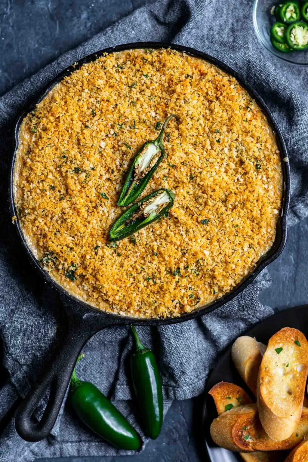 vegan jalapeño popper dip baked in cast iron with a bread crumb topping and served with crostini