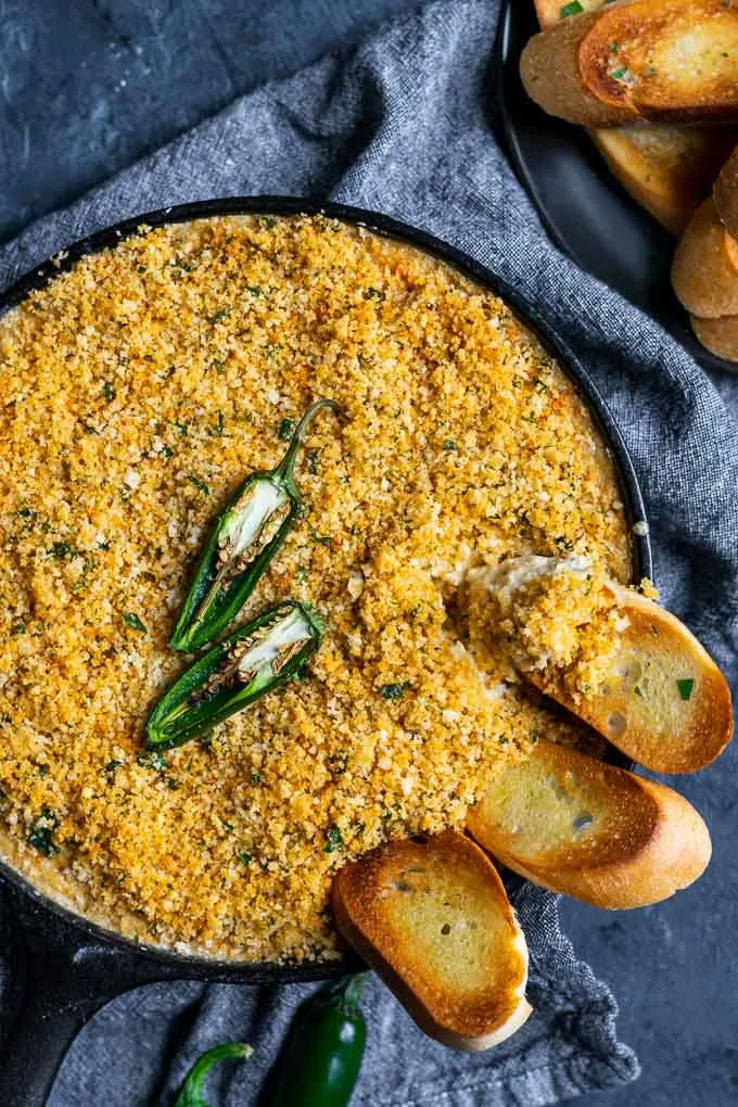 vegan jalapeño popper dip baked in a cast iron with a breadcrumb topping and crostini dipped into the pan