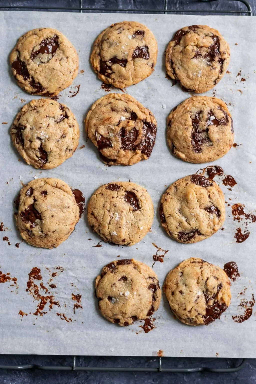 chewy vegan tahini chocolate chip cookies on parchment over a cooling rack