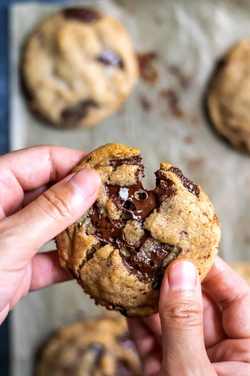 chewy vegan tahini chocolate chip cookie being broken in half in hand and with melted chocolate being pulled apart