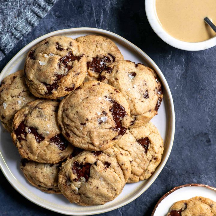 Chewy vegan tahini chocolate chip cookies on a plate with a bowl of tahini in one corner and a cookie served on a small plate in another