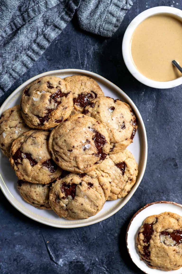 Chewy vegan tahini chocolate chip cookies on a plate with a bowl of tahini in one corner and a cookie served on a small plate in another