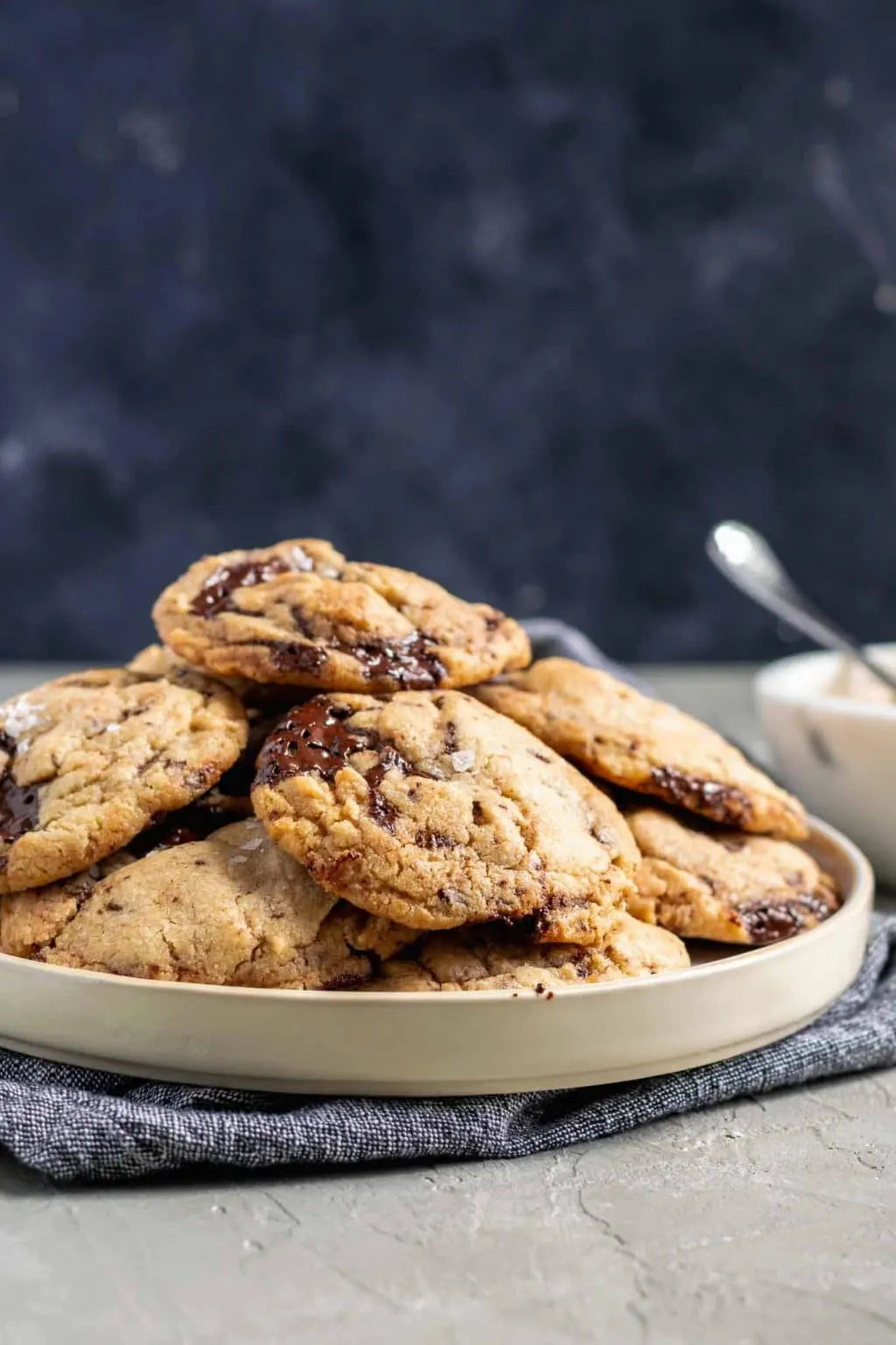 chewy vegan tahini chocolate chip cookies on a plate with a small bowl of tahini in the background