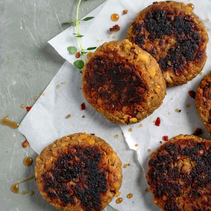 vegan tempeh maple breakfast sausage patties on a piece of parchment paper with fresh thyme, a drizzle of maple syrup, and crushed red pepper