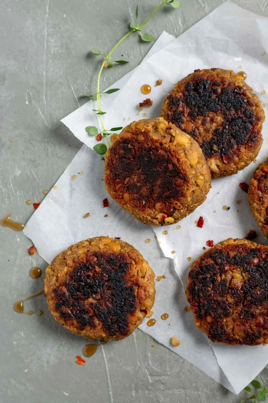 vegan tempeh maple breakfast sausage patties on a piece of parchment paper with fresh thyme, a drizzle of maple syrup, and crushed red pepper