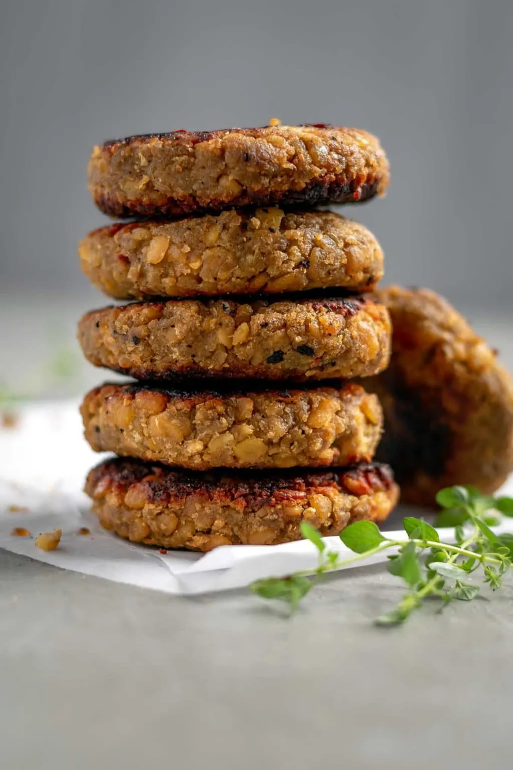 vegan tempeh maple breakfast sausage patties stacked on a piece of parchment paper with some fresh thyme and crushed red pepper for garnish