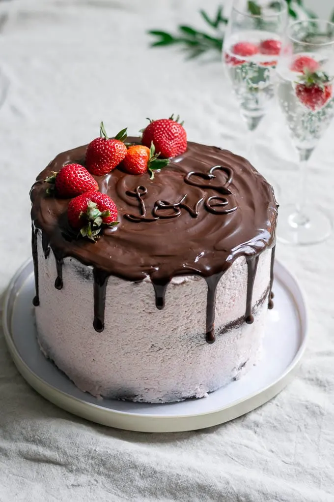 The ultimate easy vegan chocolate cake with strawberry Italian meringue buttercream, a chocolate drip, and fresh strawberries to decorate