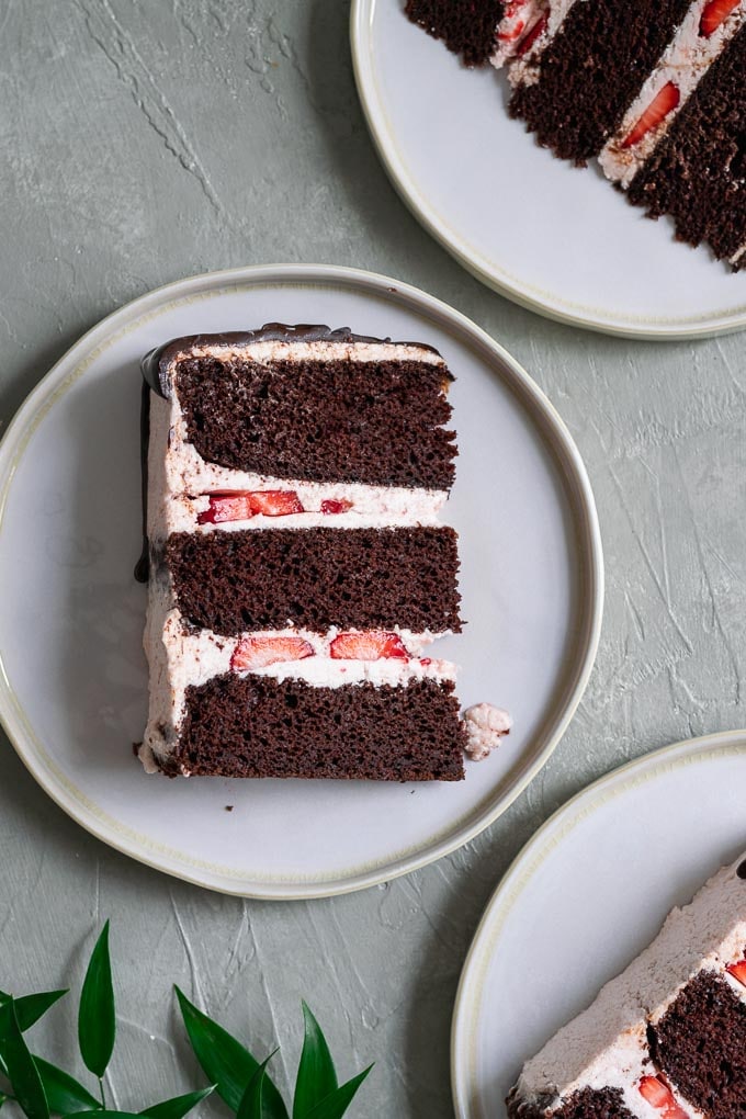 Three slices of three layer chocolate cake with vegan aquafaba strawberry Italian meringue buttercream and a chocolate drip