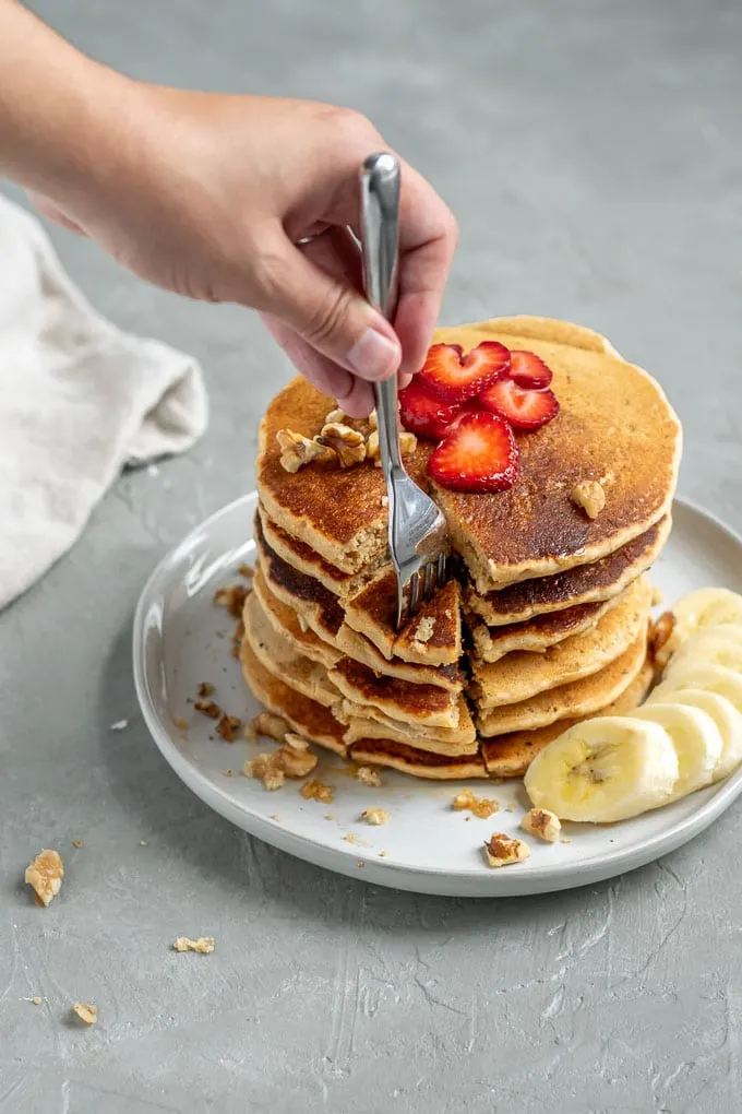 Digging a fork into whole grain cornmeal vegan pancakes cooked and stacked 6 tall