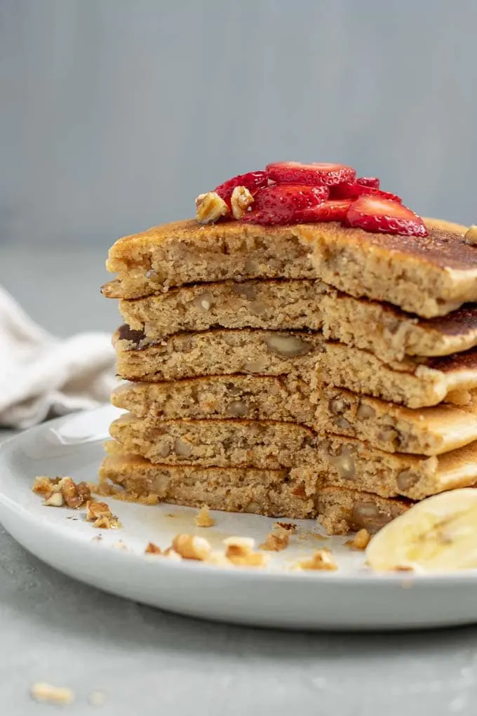 Make ahead whole grain cornmeal vegan pancake mix cooked and stacked 6 tall and sliced open to show the fluffy texture and chopped walnuts