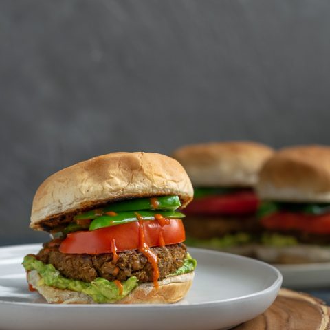 vegan curry seitan and black-eyed pea burgers with mashed avocado, sliced tomatoes, jalapeños, and hot sauce