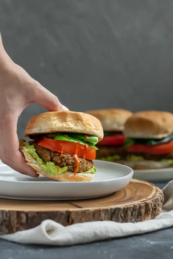 picking up vegan curry seitan and black-eyed pea burgers with mashed avocado, sliced tomatoes, jalapeños, and hot sauce