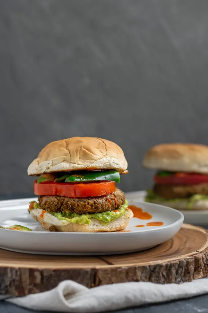 vegan curry seitan and black-eyed pea burgers with mashed avocado, sliced tomatoes, jalapeños, and hot sauce