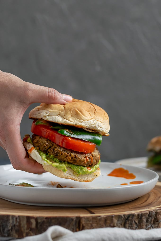 picking up vegan curry seitan and black-eyed pea burgers with mashed avocado, sliced tomatoes, jalapeños, and hot sauce