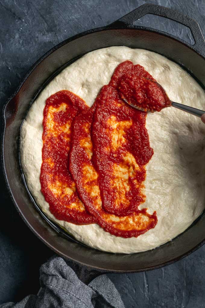 assembling vegan pepperoni pan pizza, spooning on the sauce