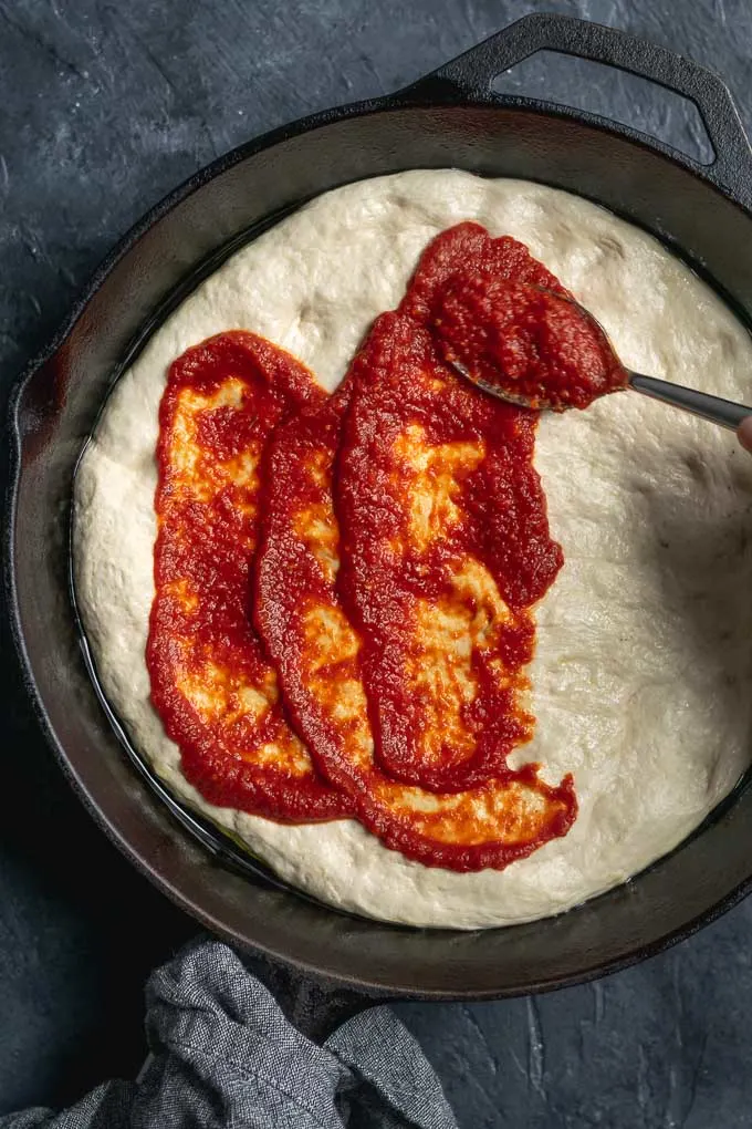 assembling vegan pepperoni pan pizza, spooning on the sauce