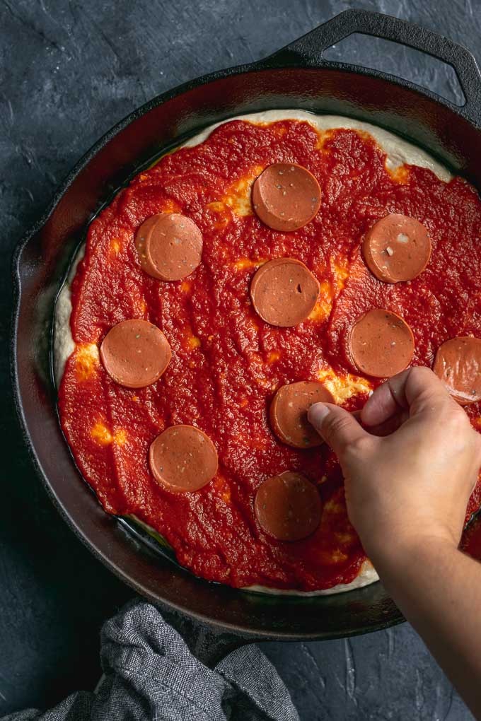 assembling vegan pepperoni pan pizza, placing the vegan pepperoni on the sauce
