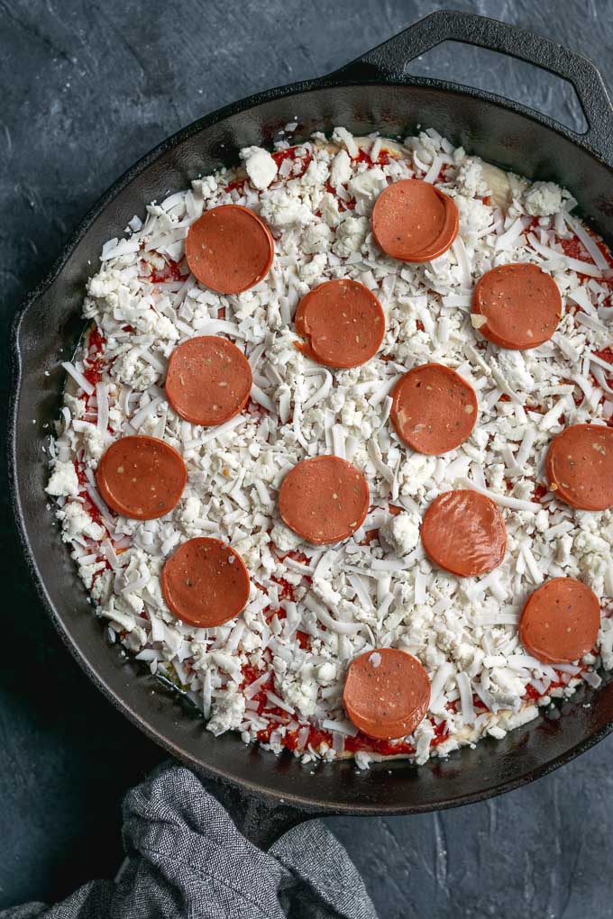 assembling vegan pepperoni pan pizza, topped with vegan mozzarella and additional vegan pepperoni