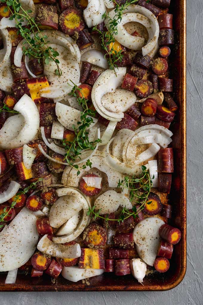 carrots, onion, garlic, thyme, and dried sage on a baking tray before roasting for easy vegan roasted carrot soup