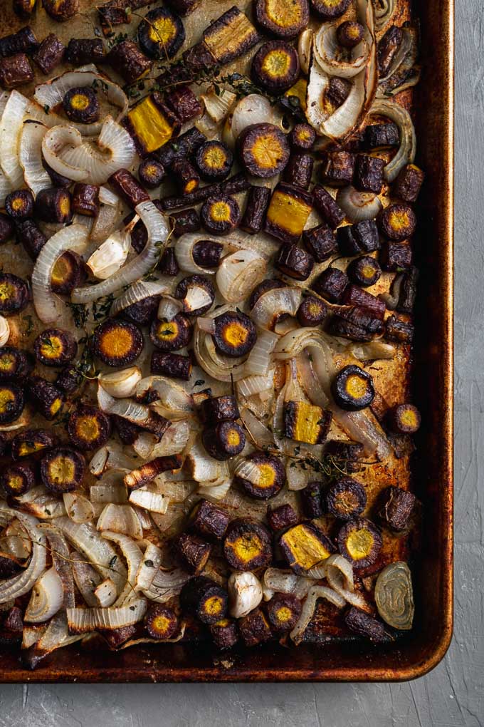 carrots, onion, garlic, thyme, and dried sage on a baking tray and roasted for easy vegan roasted carrot soup