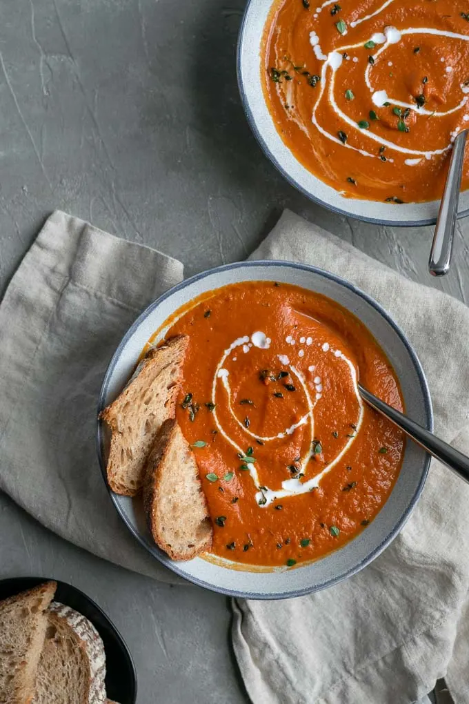 easy vegan roasted carrot soup with a drizzle of coconut milk and garnish of fresh thyme and served with sourdough toast