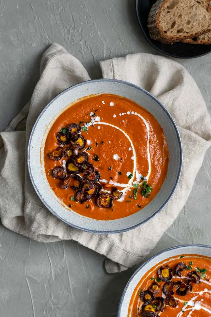 easy vegan roasted carrot soup with purple carrot chips and a drizzle of coconut milk and garnish of fresh thyme served with sourdough toast