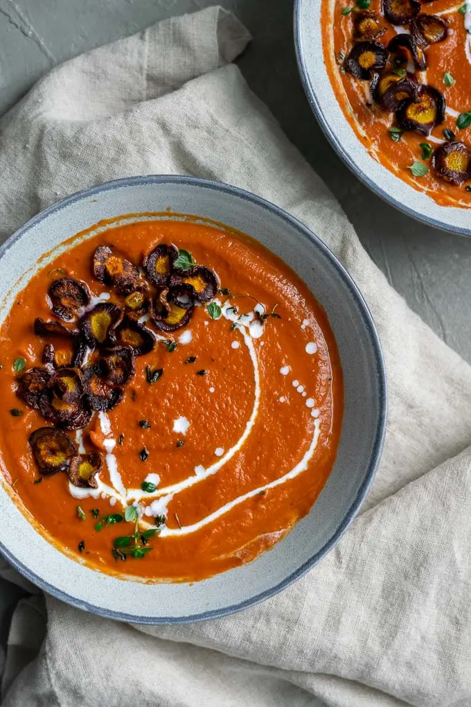 easy vegan roasted carrot soup with purple carrot chips and a drizzle of coconut milk and garnish of fresh thyme