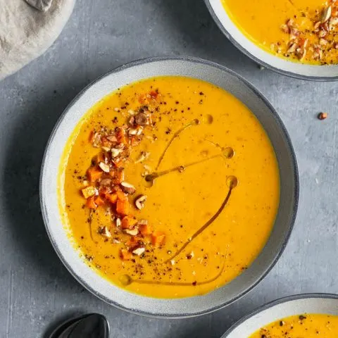 Butternut squash almond bisque with garnish of roasted squash, toasted, chopped almonds and hazelnuts, and a drizzle of olive oil